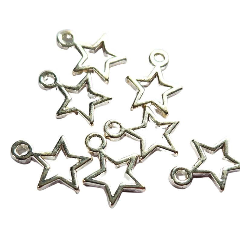 May include: Silver star charms with a hollow centre and a small loop at the top for stringing. These charms are suitable for jewellery making, scrapbooking, or other craft projects. The charms are scattered on a white background.