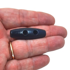 May include: Black wooden toggle button with two holes. The button is oval shaped and has a smooth finish.