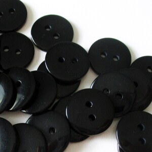 May include: A pile of black plastic buttons with two holes each. The buttons are round and smooth.