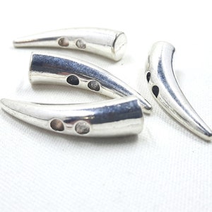 May include: Four silver metal horn-shaped buttons with two holes each. The buttons are designed to look like animal horns.