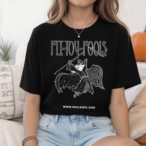 May include: Black t-shirt with the text "FLY YOU FOOLS" in a distressed white font. Below the text is a white graphic of a winged figure holding a spear. The website www.paulsimic.com is printed below the graphic.