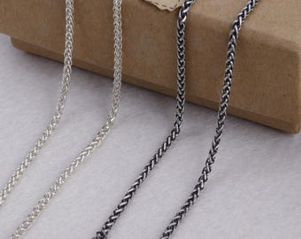 May include: Close-up of three silver-toned chain necklaces with a wheat or herringbone pattern. The chains are displayed against a neutral background, showcasing their intricate design and metallic sheen. One chain has a lobster clasp.