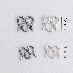 May include: Four metal hook and eye clasps in silver and dark gray. Two clasps are 18mm in length, and two are 15mm. The clasps have a wavy, interlocking design, suitable for jewelry or garment closures.