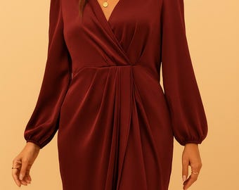 May include: A burgundy-colored dress with long sleeves and a V-neckline. The dress features a wrap-style design with a gathered detail at the waist and a thigh-high slit. The sleeves have a slight puff at the shoulders.