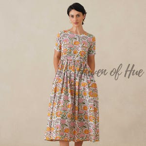 May include: A white midi dress with a floral pattern in shades of pink, yellow, and green. The dress has short sleeves and a gathered waist. The text "Maven of Hue" is visible on the right side of the image.