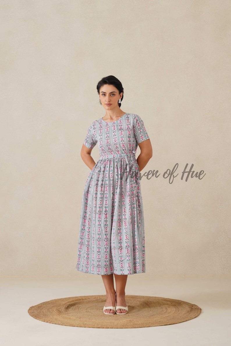 May include: A light blue dress with a vertical striped pattern of pink floral accents. The dress has short sleeves and a cinched waist. The text "Raven of Hue" is visible on the right side of the image.