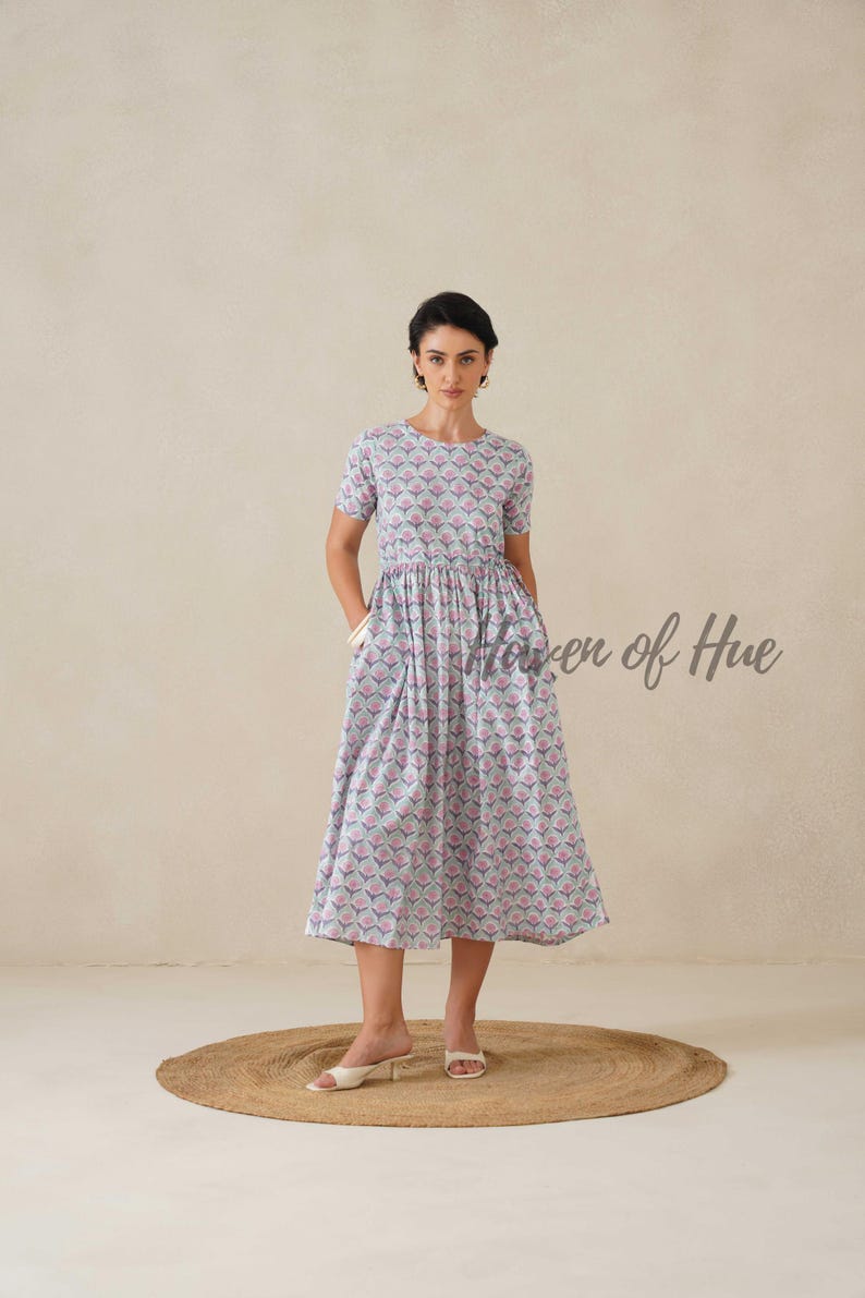 May include: A light blue midi dress with a repeating pink and blue geometric pattern. The dress has short sleeves, a round neckline, and pockets. The text "Haven of Hue" is visible on the right side of the dress.