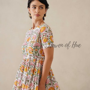 May include: A white dress with a floral pattern in shades of yellow, pink, and green. The dress has short sleeves and a fitted bodice that flares into a full skirt. The text "Haven of Hue" is visible on the right side of the image.