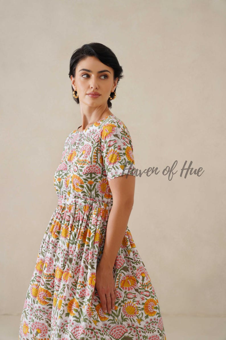 May include: A white dress with a floral pattern in shades of yellow, pink, and green. The dress has short sleeves and a fitted bodice that flares into a full skirt. The text "Haven of Hue" is visible on the right side of the image.