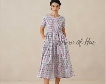 May include: A midi-length dress featuring a light blue base with a repeating pattern of small pink flower motifs. The dress has short sleeves, a round neckline, a gathered waistline, and side pockets. The text Haven of Hue is visible.