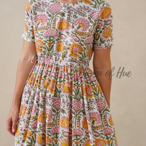 May include: A white floral print dress with short sleeves and a gathered waist. The dress features a pattern of pink and yellow flowers with green leaves. The text "en of Hue" is visible on the dress.
