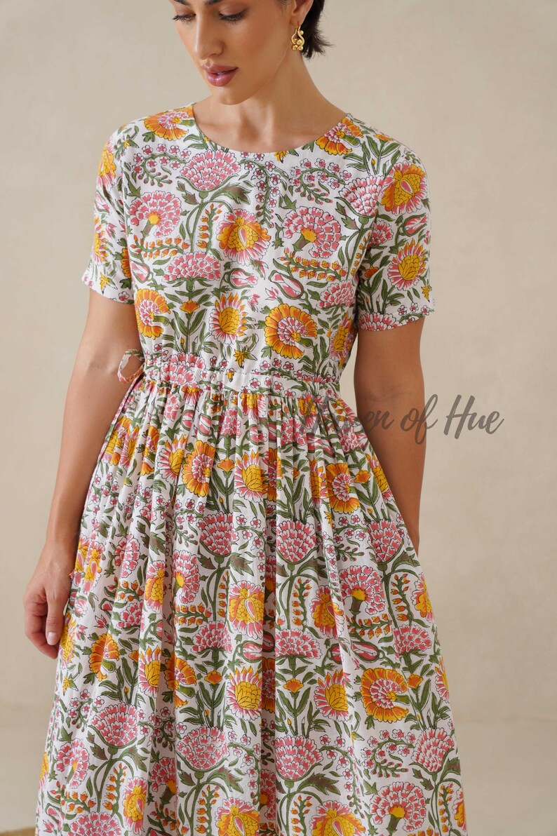 May include: A white floral print dress with short sleeves and a gathered waist. The dress features a pattern of pink and yellow flowers with green leaves. The text "en of Hue" is visible on the dress.