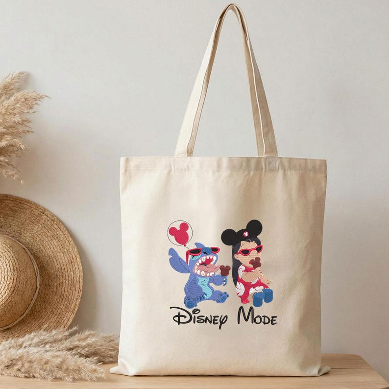 K&ouml;nnte beinhalten: Eine beige Tragetasche aus Segeltuch mit einem Grafikdruck der blauen Figur Stitch und einem M&auml;dchen, beide tragen eine rote Sonnenbrille und Haarreifen mit Mickey-Maus-Ohren. Der Text Disney Mode ist darunter in Schwarz aufgedruckt.