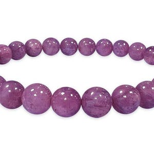 May include: A bracelet featuring round, polished beads in shades of purple. The beads are strung together to form a continuous loop. The bracelet is displayed against a white background.