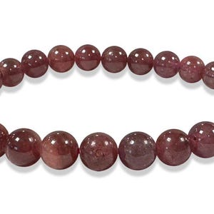 Può includere: Un braccialetto di perline rotonde e lucide, nei toni del bordeaux e del marrone. Le perline sono infilate su un elastico, mostrando le variazioni naturali di colore e consistenza della pietra. Un gioiello semplice ed elegante.