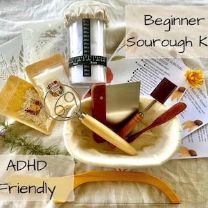 May include: A sourdough bread-making kit featuring a clear measuring container, a dough whisk, a bench scraper, and a wooden lame. The kit includes ingredient packets and instructions. The text "Beginner Sourdough Kit" and "ADHD Friendly" are visible.