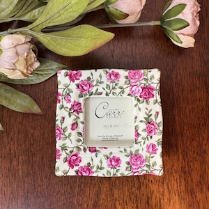 May include: A square picture frame with a cream background and a repeating pattern of pink roses and green leaves. The center insert features the text Carr Frames Since 1965, 2 1/2 x 2 1/2, From the Burnes of Boston Family of Brands.