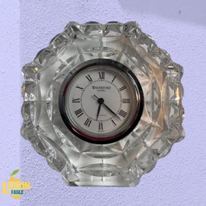 Puede incluir: Un reloj de cristal transparente con una esfera redonda con números romanos y las palabras "WATERFORD CRYSTAL". El reloj tiene un diseño facetado en forma de estrella alrededor de la esfera. El reloj está marcado "JAPAN".
