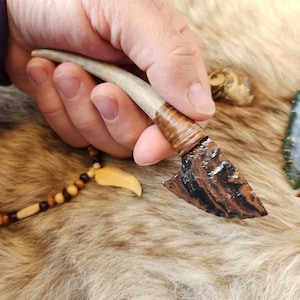 Peut inclure: Un petit couteau artisanal avec une lame en obsidienne brun foncé et un manche en bois de cerf blanc enveloppé de cuir brun.