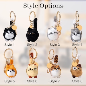May include: A collection of eight crochet cat keychains, each with a gold-colored keyring and a small, round tag. The cats vary in color and pattern, including black, white, gray, orange, and brown. The text "Style Options" is at the top, with style numbers below each cat.