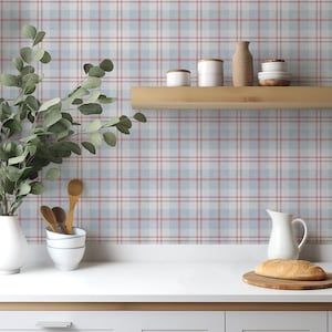 May include: A kitchen scene with a white countertop and a light blue, red, and white plaid wallpaper. A white pitcher, a wooden cutting board with bread, and a vase with greenery are on the counter. Wooden spoons and white bowls are also visible.