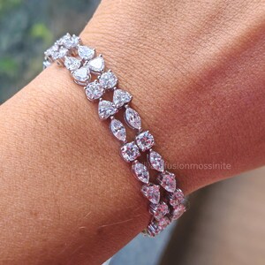 May include: A silver bracelet with multiple rows of clear, sparkling gemstones. The gemstones are cut into various shapes, including pear, marquise, and round cuts. The bracelet is worn on a wrist, showcasing its elegant design and brilliance.