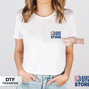 May include: White t-shirt with the "EASY DTF STORE" logo in red, blue, and white. The words "DTF TRANSFER" are in a white rectangle at the bottom left. The shirt is being held by a person wearing blue jeans.