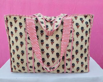 May include: A large tote bag with a cream-colored background and a repeating floral pattern in navy and red. The bag features red and white striped handles and trim, and is sitting on a white surface against a pink backdrop.
