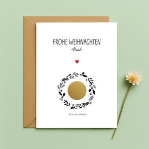 Puede incluir: Una tarjeta navideña blanca con el texto "FROHE WEIHNACHTEN Noah" en negro, un corazón rojo y un círculo dorado dentro de una corona negra y blanca. La tarjeta está en un sobre marrón.