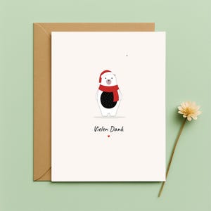 May include: A greeting card featuring a cartoon polar bear in a red scarf and Santa hat. The card reads "Vielen Dank" with a small red heart. It is presented with a brown envelope.