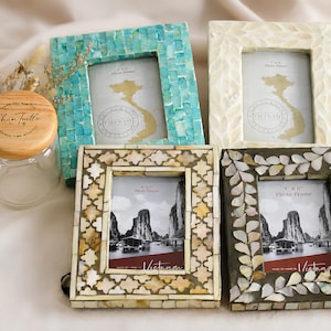Op de afbeelding: Vier rechthoekige fotolijsten met ingelegd schelppatroon in turquoise, crème en donkergrijs, naast een glazen pot met een houten deksel met het opschrift Shan Turtle. De lijsten bevatten 10x15 cm inzetstukken met Vietnam-kaarten en landschapsafbeeldingen.