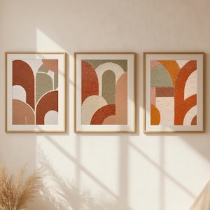 Puede incluir: Tres impresiones artísticas abstractas enmarcadas con diseños geométricos en tonos óxido, beige y verde oliva. La obra de arte se exhibe en una pared neutra, con una cesta y una alfombra tejidas en primer plano, creando una estética cálida y acogedora.