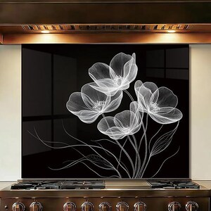 Könnte beinhalten: Schwarze Küchenrückwand aus Glas mit weißem Blumendesign. Das Kunstwerk zeigt eine Ansammlung zarter, durchscheinender Blumen mit detaillierten Linien und Stielen. Die Rückwand ist über einem Gasherd aus Edelstahl installiert.