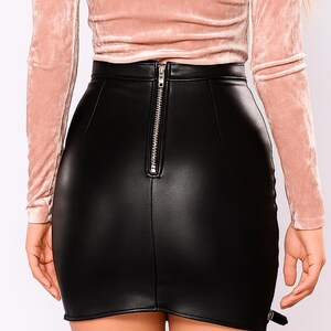 May include: A black, faux leather mini skirt with a high waist and a silver zipper down the back. The skirt has a fitted silhouette and a small buckle detail on the side.