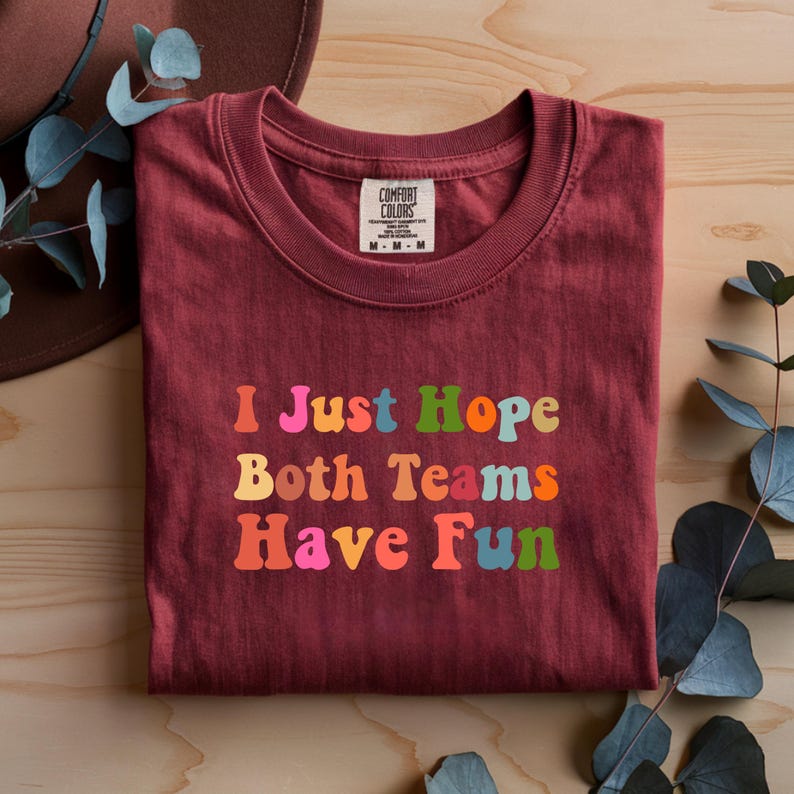 Peut inclure: Un t-shirt bordeaux avec l'inscription "I Just Hope Both Teams Have Fun" en lettres color&eacute;es de style r&eacute;tro. Le t-shirt a un col rond et une &eacute;tiquette "Comfort Colors".