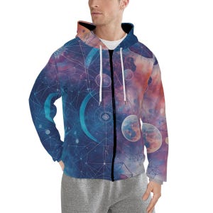 May include: A zip-up hoodie with a celestial design. The jacket features a vibrant print of planets, constellations, and geometric shapes in shades of blue, purple, and orange. The hoodie has a white drawstring and a black zipper.