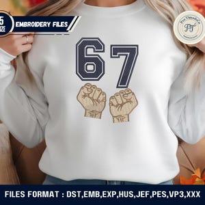 May include: White sweatshirt with the number "67" in navy blue, featuring two embroidered fists. The design includes the text "EMBROIDERY FILES" and "Pro Threads Co." in a circular logo. The bottom of the image displays "FILES FORMAT : DST, EMB, EXP, HUS, JEF, PES, VP3, XXX".