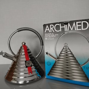 May include: A stainless steel conical kettle with a ribbed texture, a coiled handle, and a star-shaped spout cover. A red ribbon with a black tag hangs from the handle. Next to it is a box labeled ARCHIMEDE BOLLITORE IN ACCIAIO INOX 18/10 CON FISCHIETTO STELLA 1 LITRO.
