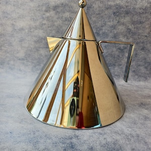 May include: A polished stainless steel stovetop espresso maker with a conical body and a small handle. The espresso maker has a small ball on top and reflects the surrounding environment. The product is designed for brewing coffee.