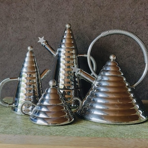 Op de afbeelding: Een verzameling van vier gepolijste zilveren theepotten met unieke, conische ontwerpen. De theepotten variëren in grootte en vorm, sommige met steraccenten en spiraalvormige handvatten. Ze staan op een groene ondergrond tegen een donkerbruine achtergrond.