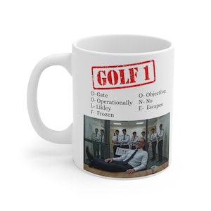 Könnte beinhalten: Weiße Keramik-Tasse mit dem Text "GOLF 1" in einem roten Stempeldesign. Die Tasse enthält auch eine Liste von Akronymen und ein humorvolles Bild eines liegenden Mannes. Ein tolles Geschenk für einen Freund oder ein Familienmitglied.