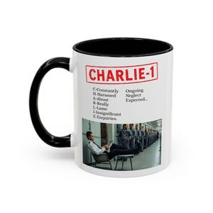 Può includere: Tazza in ceramica bianca con manico e interno neri. La tazza presenta il testo "CHARLIE-1" in un rettangolo rosso, insieme a un elenco di parole e una foto di un uomo che legge un giornale. La tazza è un oggetto di novità.
