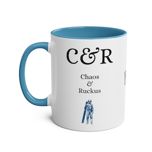 Könnte beinhalten: Weißer Keramikbecher mit blauem Innenraum und Griff. Der Becher trägt den schwarzen Text "C&R Chaos & Ruckus" sowie eine blaue Illustration einer Person, die einen langen Gegenstand hält. Ein lustiges und einzigartiges Geschenk.