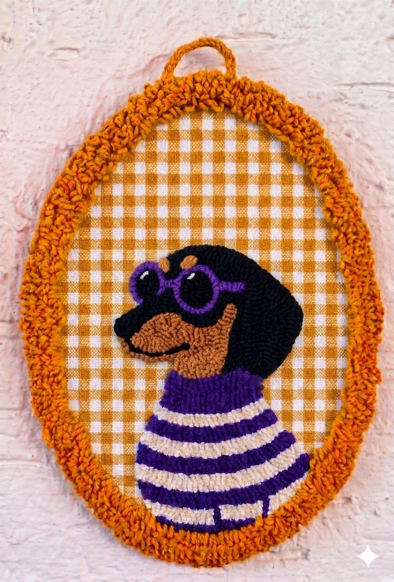 May include: An oval punch needle wall hanging featuring a black and tan dachshund wearing purple round glasses and a purple and white striped sweater. The dog is centered on a yellow and white gingham fabric background with a textured orange border.