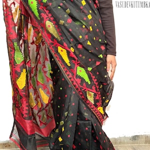 May include: Black saree with intricate red, yellow, and green embroidered patterns. The saree features a detailed border and a sheer, flowing fabric. The design includes floral and geometric motifs.