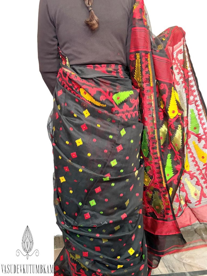 May include: A black sari with a vibrant red, yellow, and green patterned border and accents. The sari features a repeating pattern of colorful floral and geometric shapes. The fabric appears sheer and lightweight, with a decorative edge.