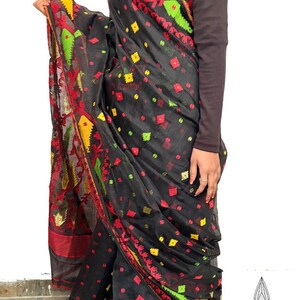 May include: Black saree with red, yellow, and green floral and geometric patterns. The saree has a decorative border with intricate designs. The fabric appears to be lightweight and flowing, with a subtle sheen.