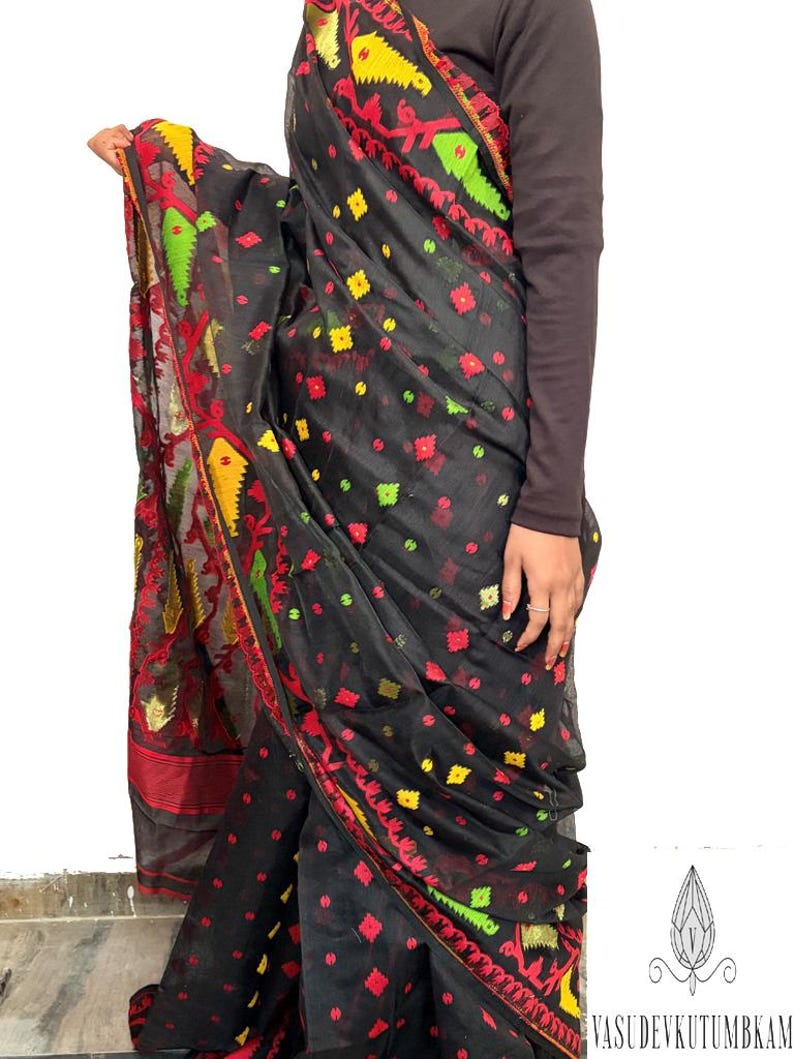 May include: Black saree with red, yellow, and green floral and geometric patterns. The saree has a decorative border with intricate designs. The fabric appears to be lightweight and flowing, with a subtle sheen.