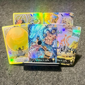 May include: Six trading cards with anime character illustrations. Each card has the number "5000" in the corners. The cards are displayed on a dark surface. The cards feature Japanese text.