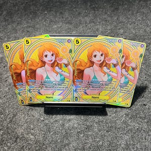 May include: A set of trading cards featuring the character Nami. Each card has a yellow background with a portrait of Nami, the number 5, and the number 6000. The cards are displayed on a dark grey surface.